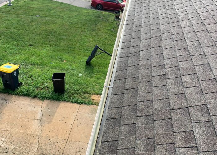 Technician clearing leaves from clogged gutter on home in Kansas City, MO