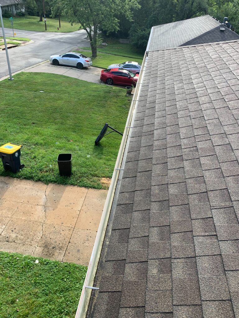 Technician clearing leaves from clogged gutter on home in Kansas City, MO